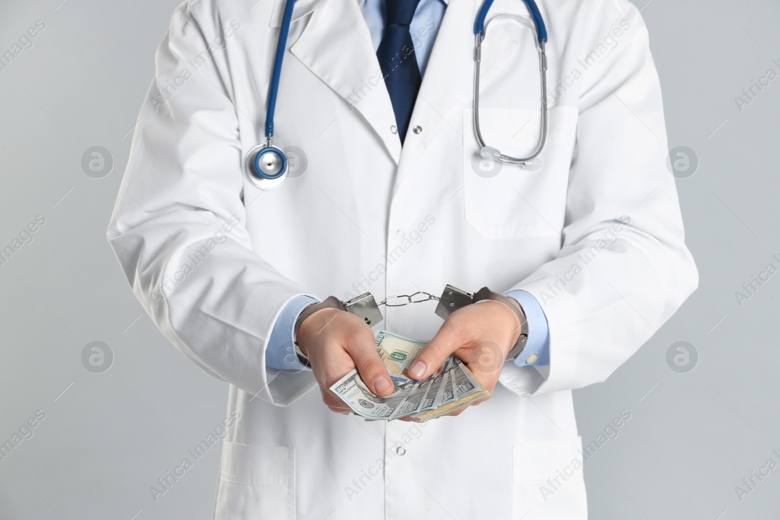 Photo of Doctor in handcuffs with bribe on grey background, closeup. Corrupted medicine