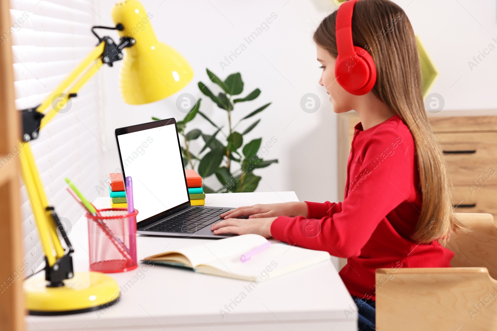 Photo of E-learning. Girl using laptop and headphones during online lesson at table indoors