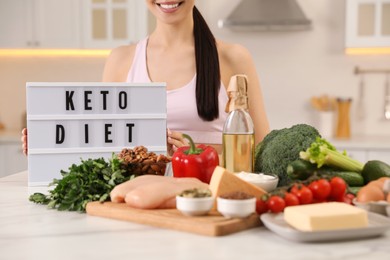 Photo of Happy woman near lightbox with words Keto Diet and different products in kitchen, closeup