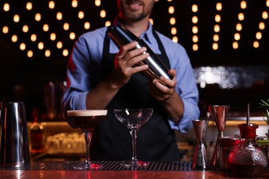 Photo of Bartender with shaker preparing fresh alcoholic cocktail in bar, closeup