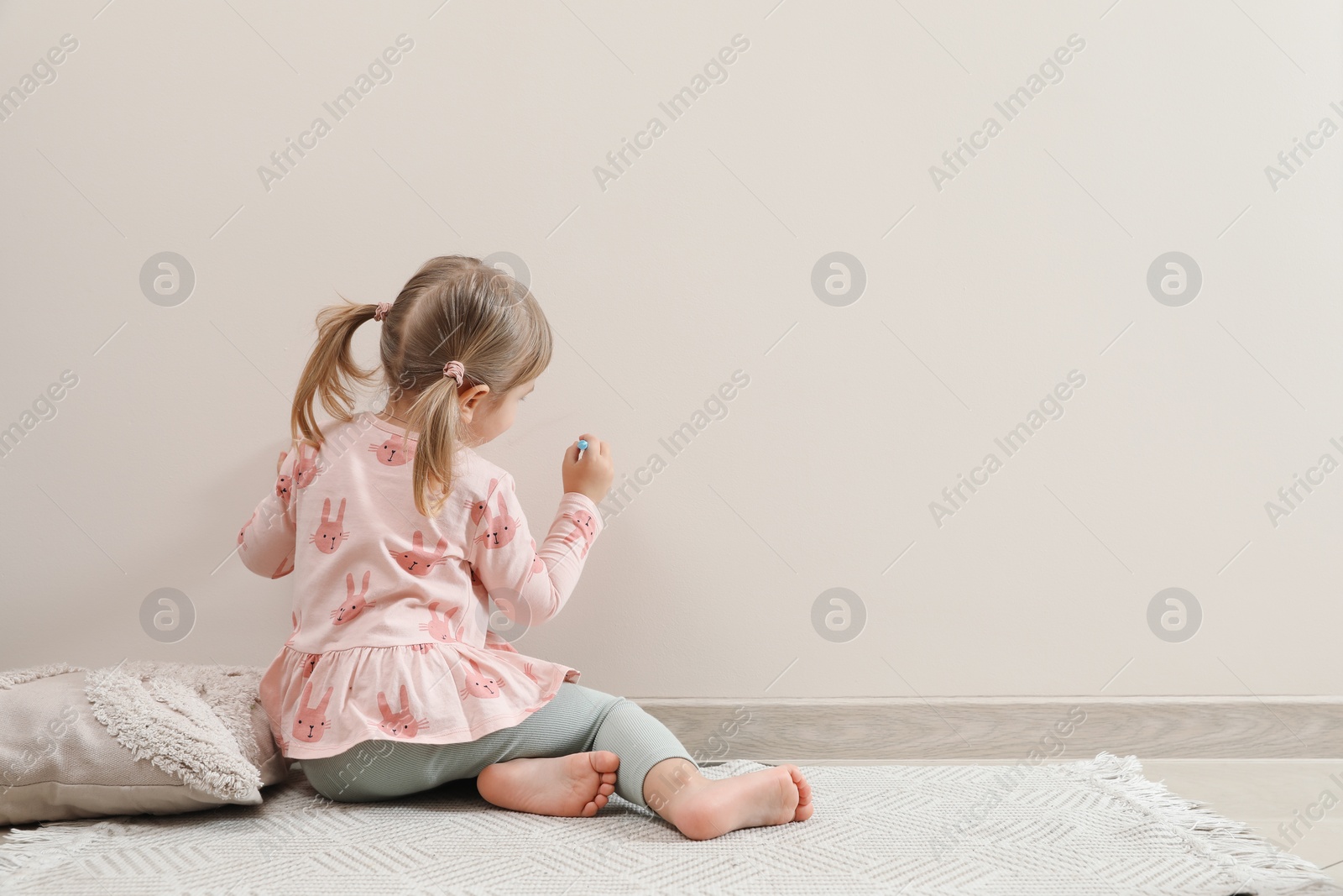 Photo of Little girl drawing on beige wall indoors, back view and space for text. Child`s art