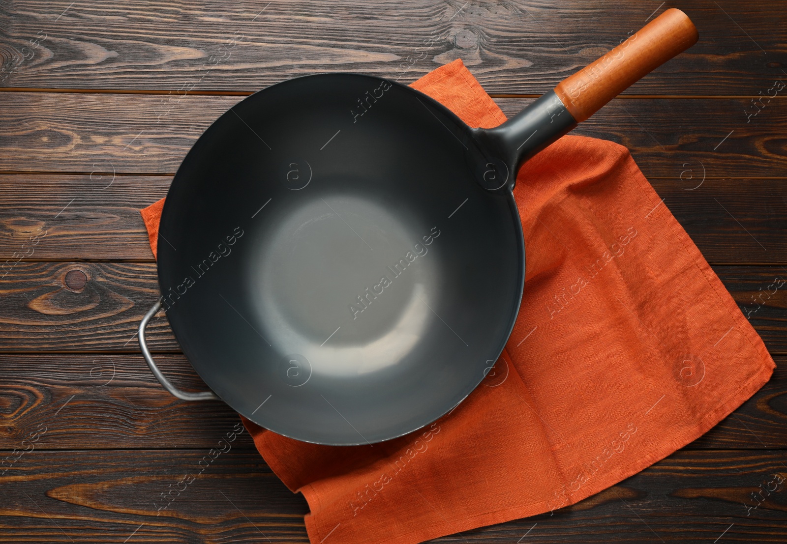 Photo of Empty iron wok with napkin on wooden table, top view