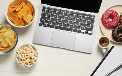 Photo of Bad eating habits at workplace. Laptop and different snacks on white wooden table, flat lay