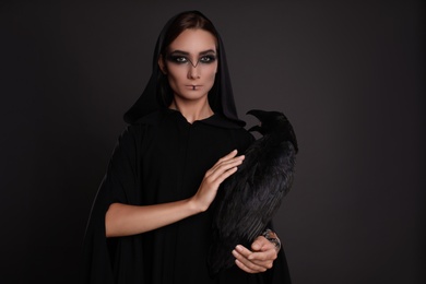 Photo of Mysterious witch with raven on black background