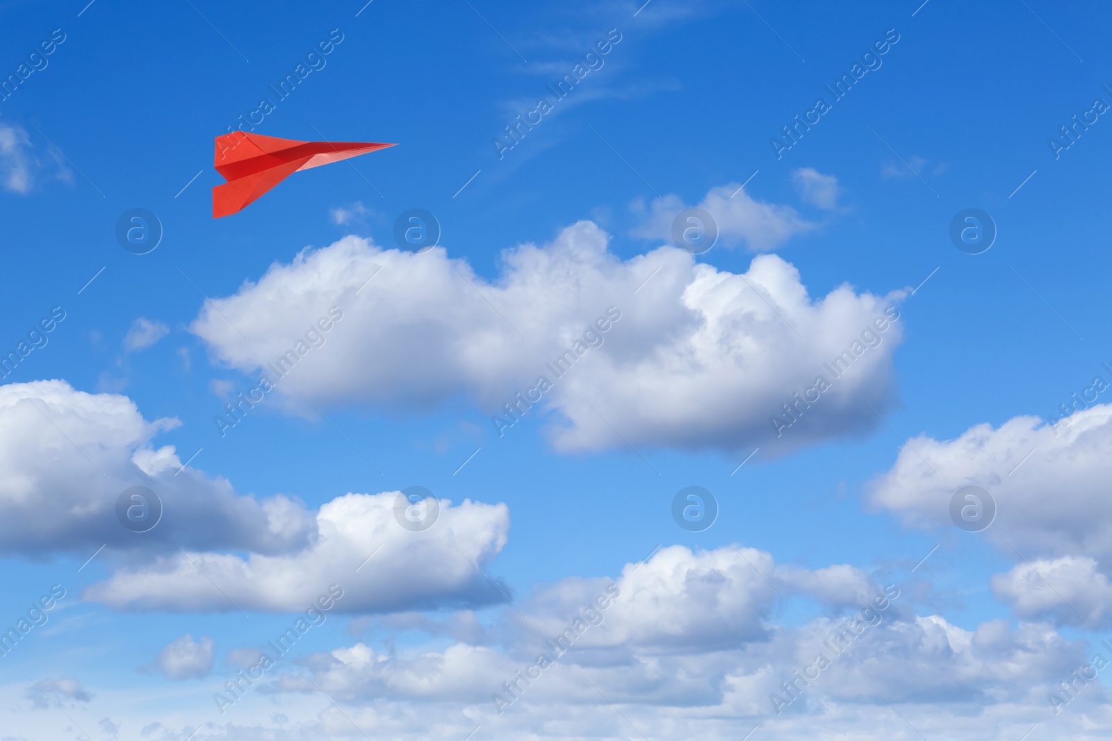 Image of Red paper plane flying in blue sky with clouds