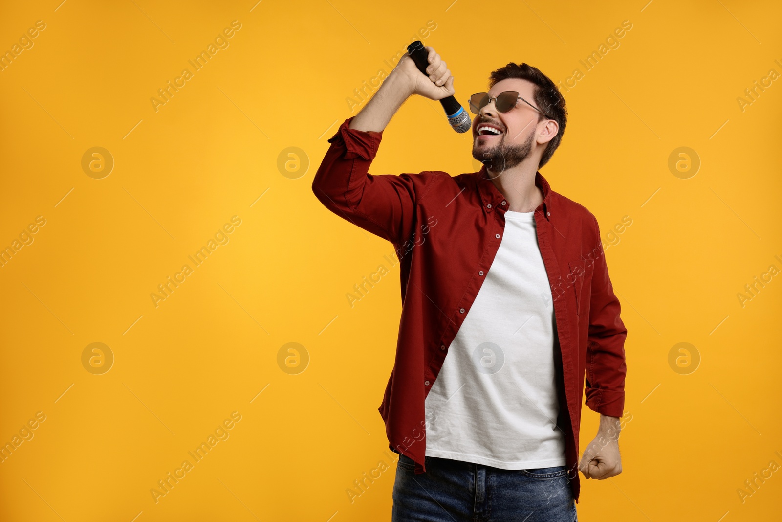 Photo of Handsome man with sunglasses and microphone singing on yellow background