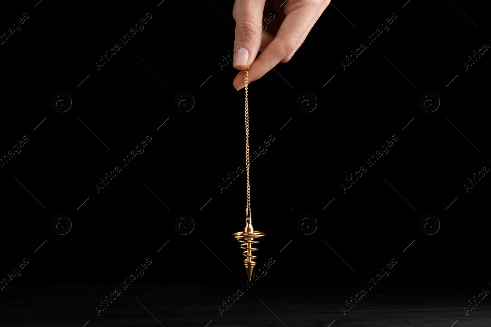 Photo of Psychotherapist with pendulum on black background, closeup. Hypnotherapy session