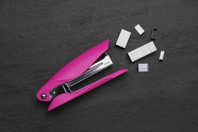 Photo of New bright stapler with staples on black table, fat lay. School stationery