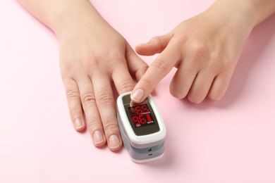 Photo of Woman using fingertip pulse oximeter on pink background, closeup