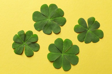 Photo of Green four leaf clover on yellow background, flat lay