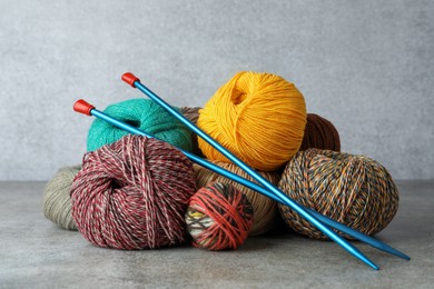 Soft woolen yarns and knitting needles on grey table