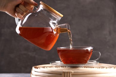 Woman pouring freshly brewed tea into glass cup on wicker table, closeup