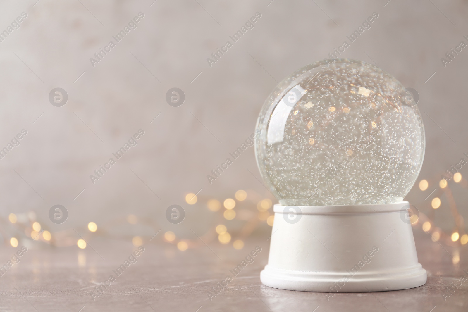 Photo of Snow globe on marble table against festive lights, space for text. Christmas season