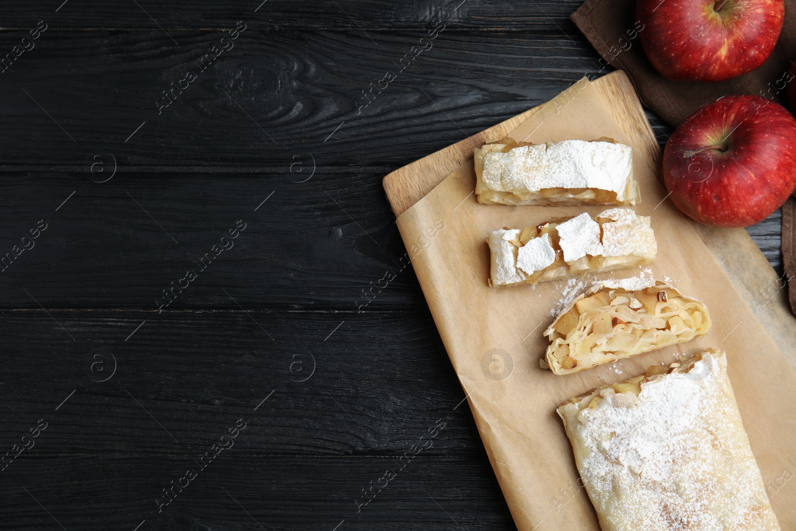 Photo of Delicious strudel and fresh apples on black wooden table, flat lay. Space for text