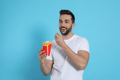 Photo of Man with French fries on light blue background, space for text