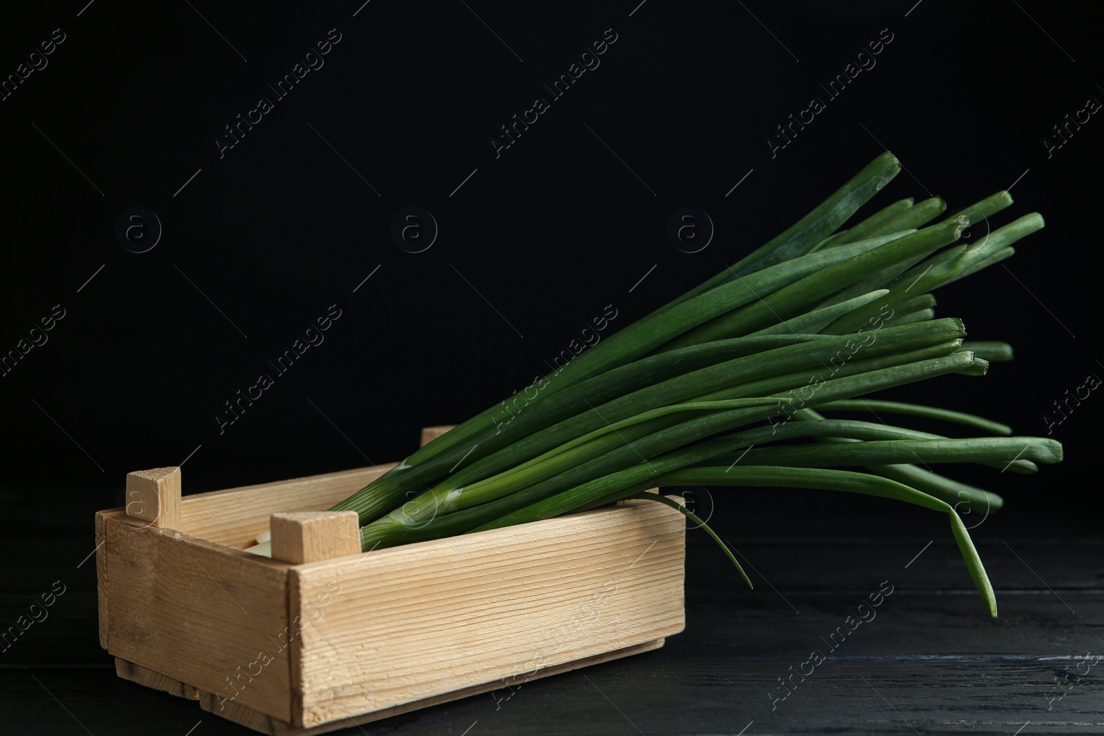 Photo of Fresh green spring onions in crate on black wooden table