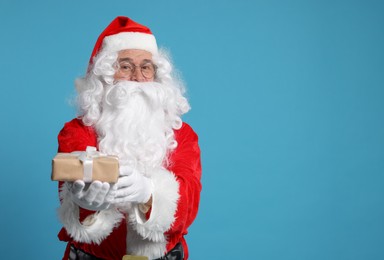 Photo of Santa Claus holding Christmas gift on light blue background, space for text