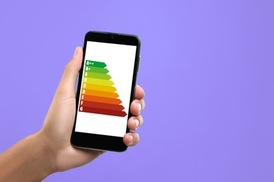 Image of Energy efficiency rating on smartphone display. Man holding device on violet background, closeup