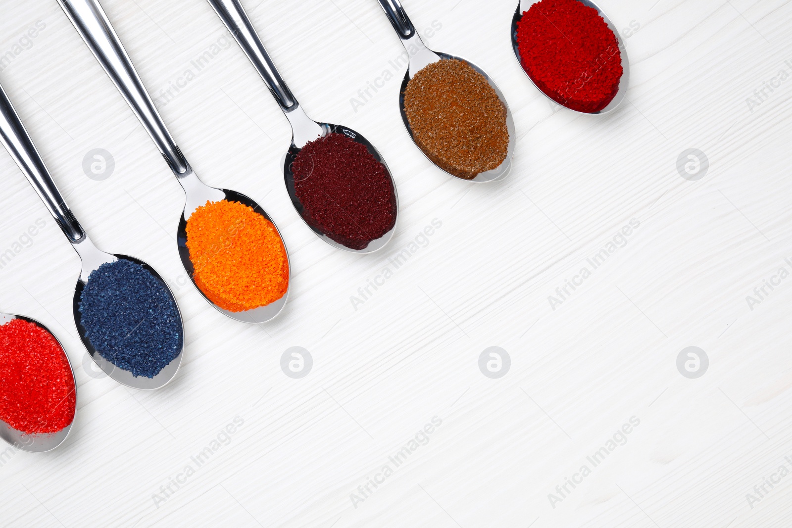 Photo of Spoons with different food coloring on white wooden table, flat lay. Space for text