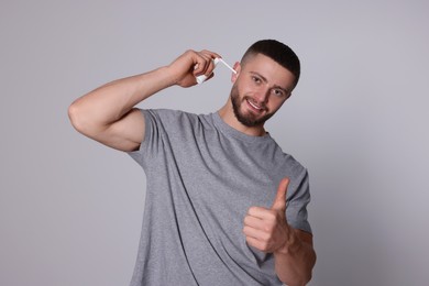 Photo of Happy man using ear spray and showing thumb up on light grey background