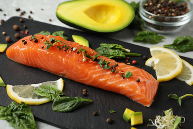 Photo of Delicious salmon served with spinach, lemon and avocado on slate board, closeup