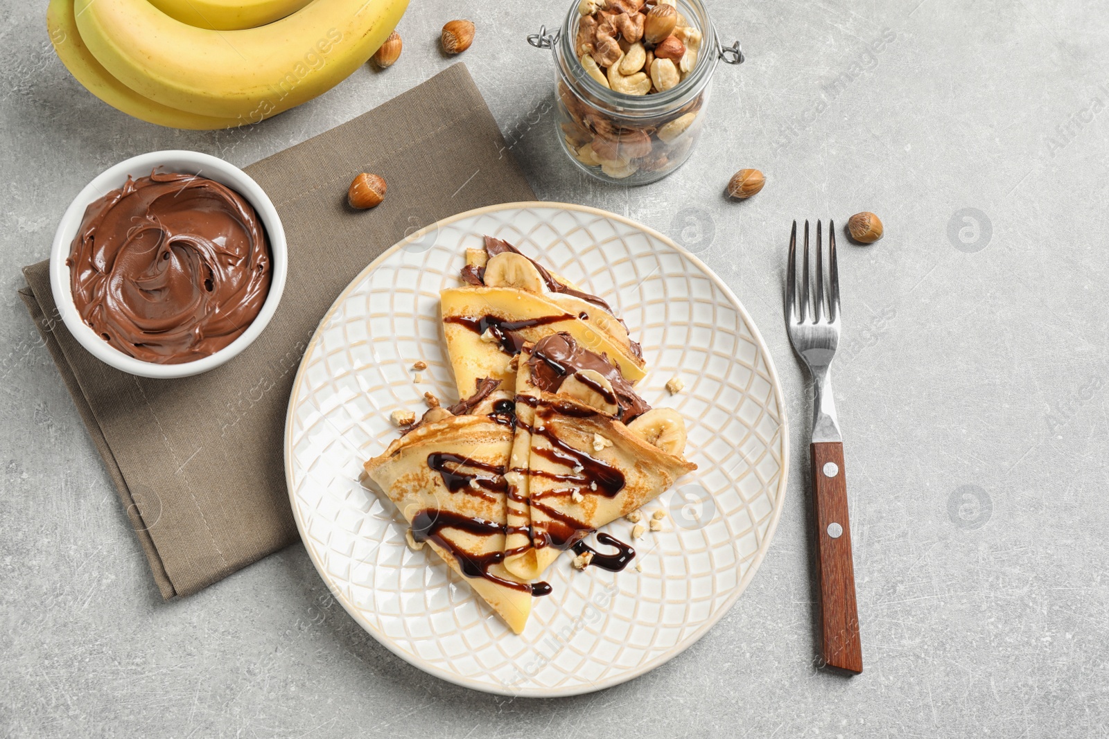 Photo of Delicious thin pancakes with chocolate spread, banana and nuts on light table, flat lay