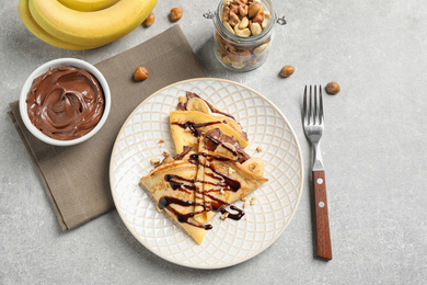 Photo of Delicious thin pancakes with chocolate spread, banana and nuts on light table, flat lay