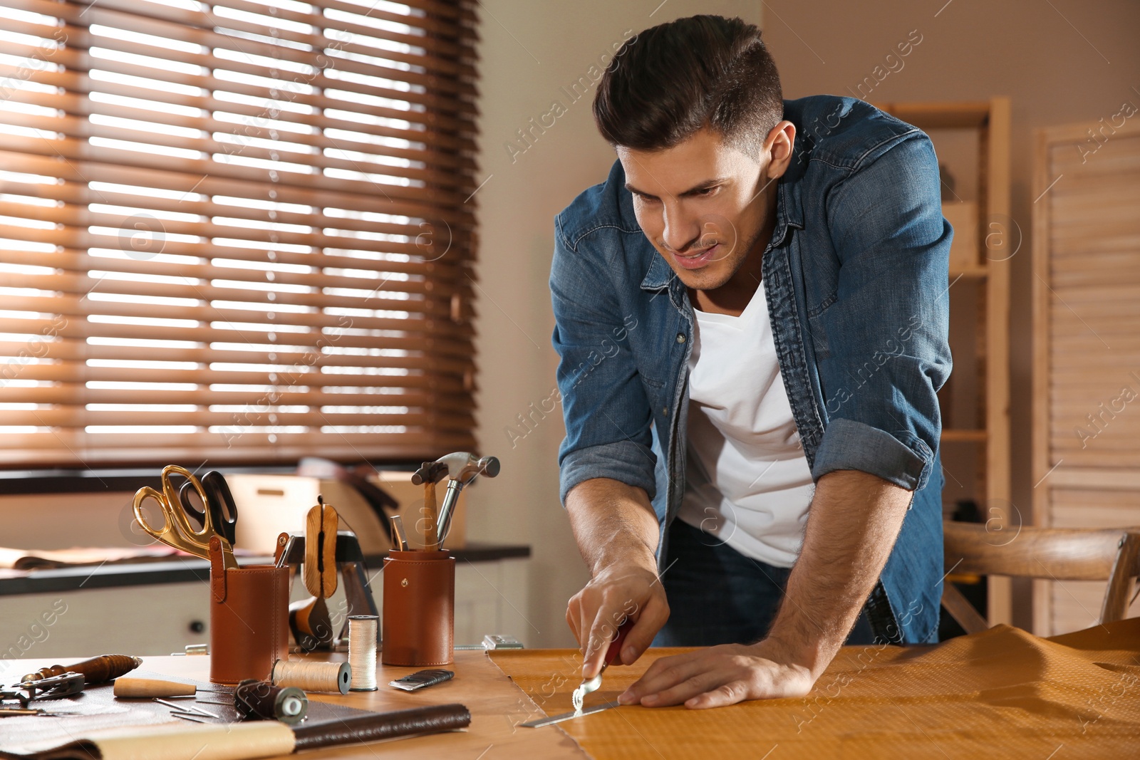 Photo of Man marking leather with roller in workshop