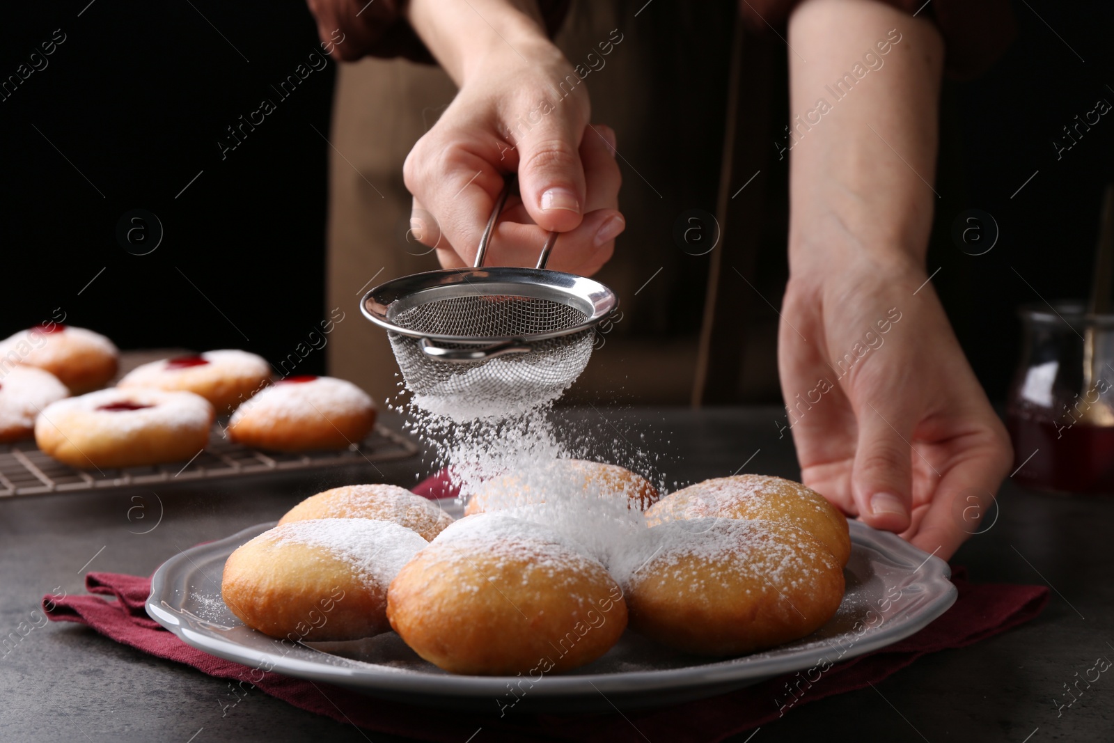 Photo of Woman dusting powdered sugar onto delicious Hanukkah donuts on grey table, closeup