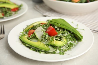 Photo of Delicious vegetable salad with avocado and microgreens served on light table
