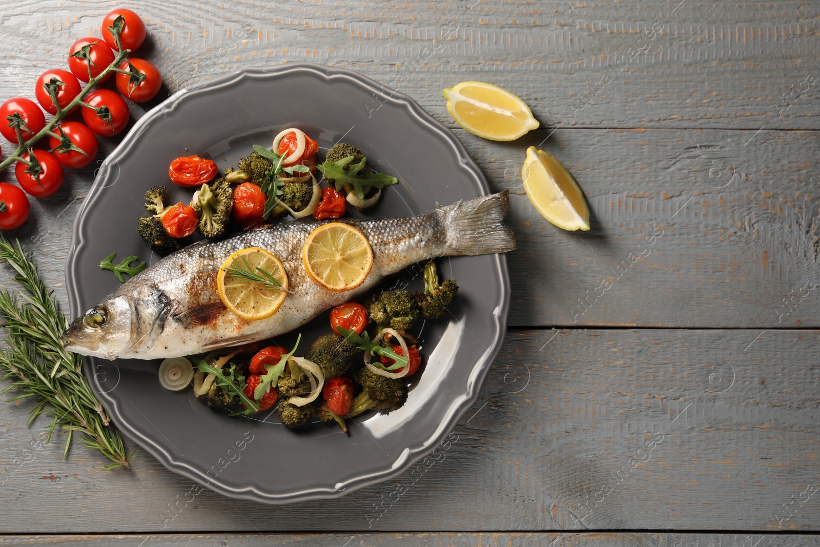 Photo of Baked fish with vegetables, rosemary and lemon on grey wooden table, flat lay. Space for text