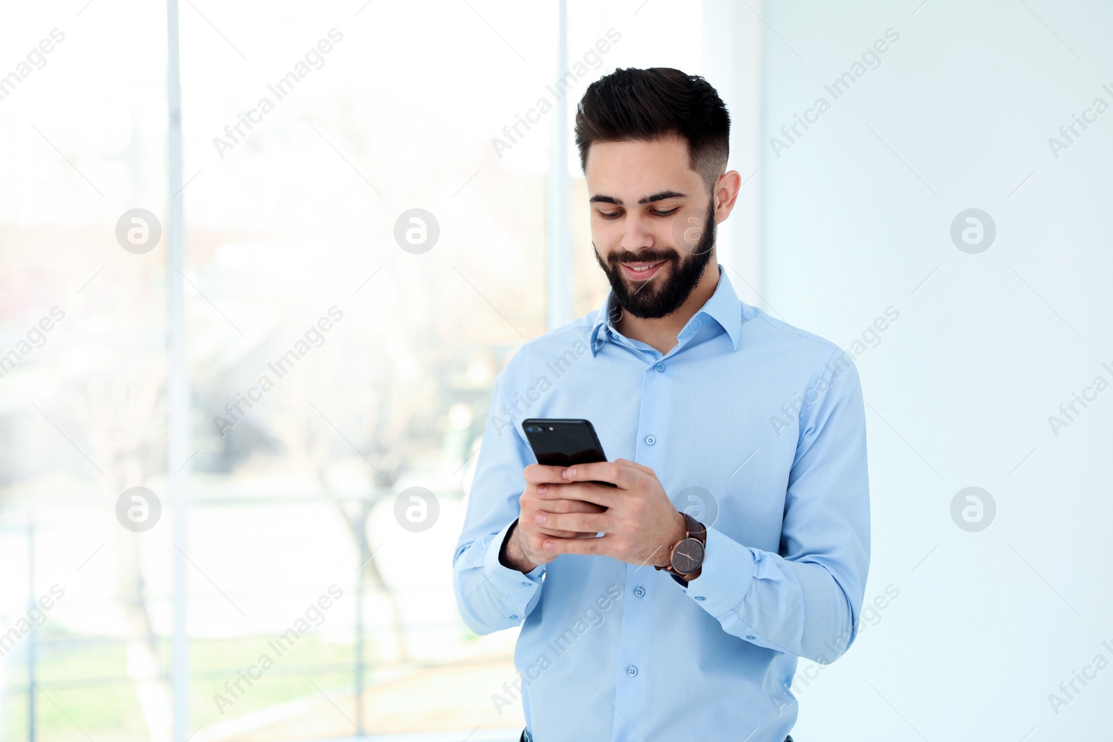 Photo of Handsome young man using phone in light room, space for text. Working time