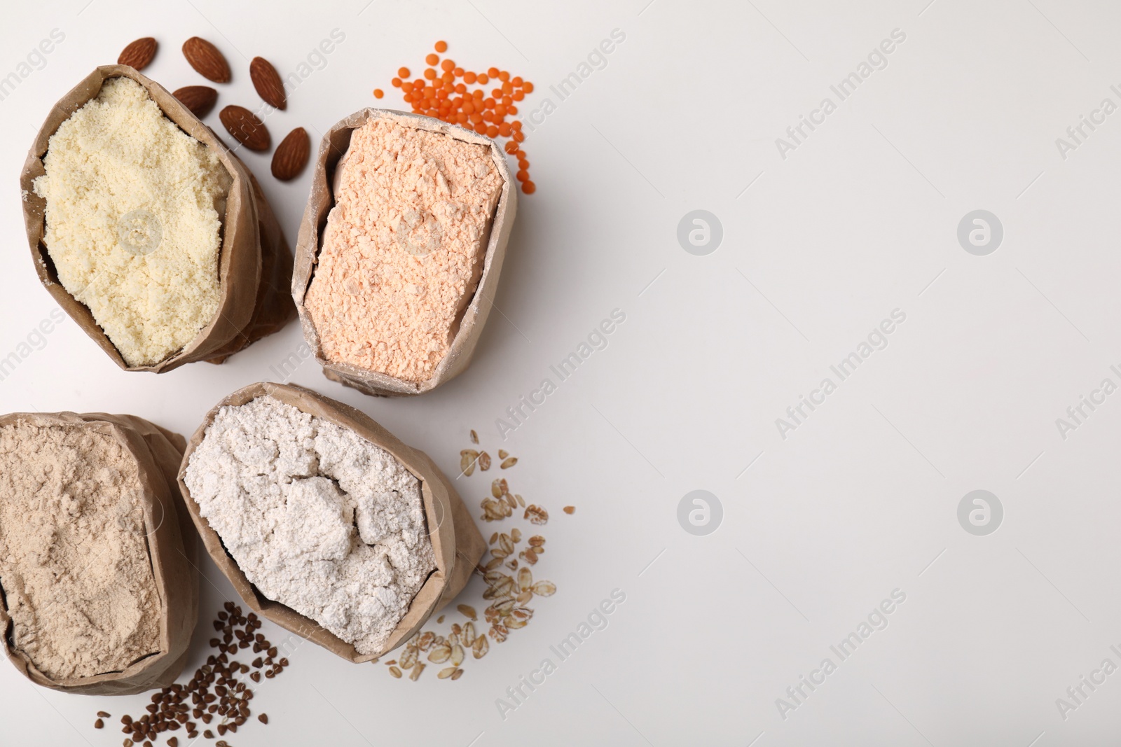 Photo of Paper bags with different types of flour on white background, top view. Space for text