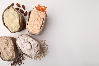 Paper bags with different types of flour on white background, top view. Space for text