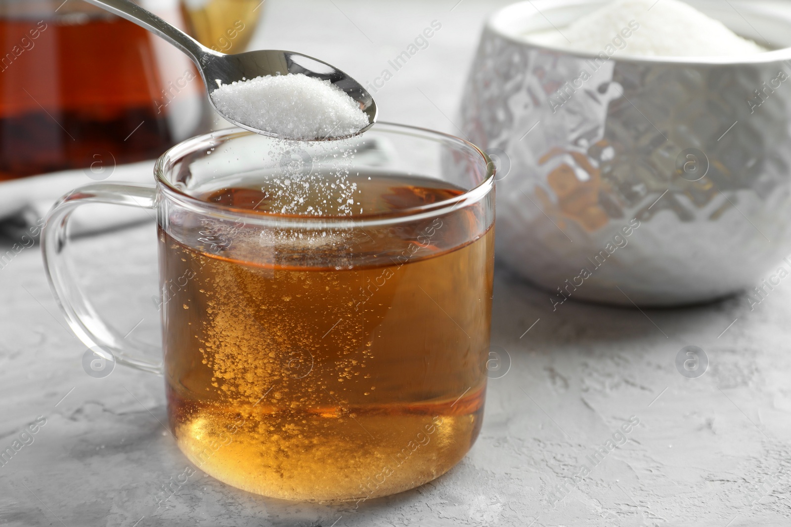 Photo of Adding sugar into cup of tea at grey textured table, closeup