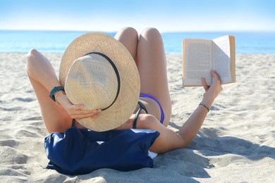 Photo of Woman reading book on sandy beach near sea