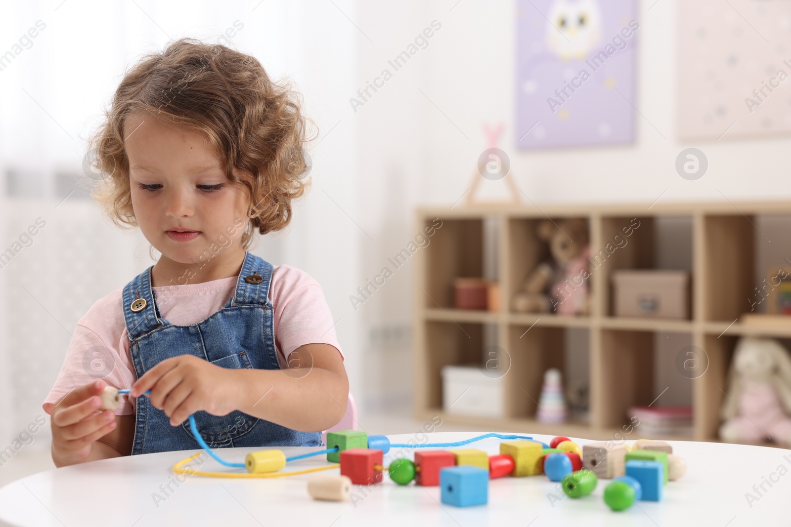 Photo of Motor skills development. Little girl playing with wooden pieces and string for threading activity at table indoors