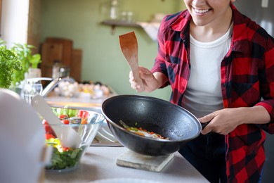 Photo of Young woman holding pan with freshly fried eggs and vegetables in kitchen, closeup