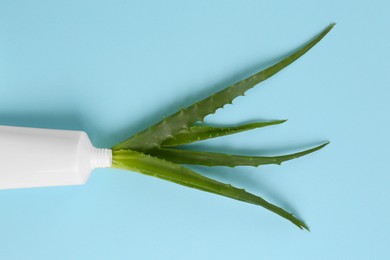 Tube of toothpaste and fresh aloe on light blue background, top view