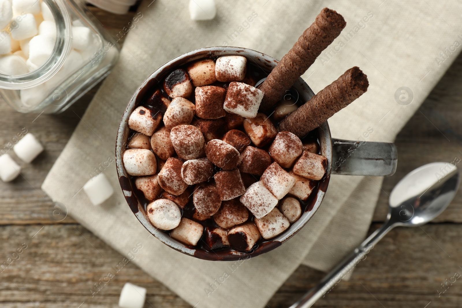 Photo of Delicious hot chocolate with marshmallows and cocoa powder in cup on wooden table, flat lay