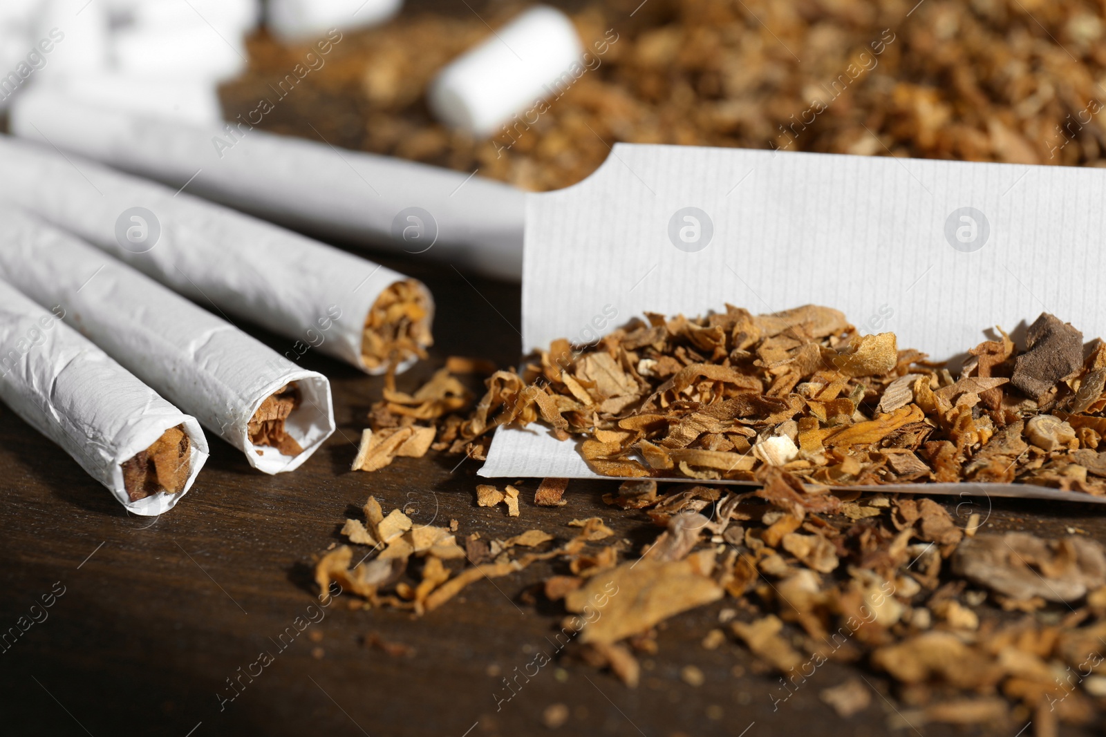 Photo of Tobacco and hand rolled cigarettes on wooden table, closeup