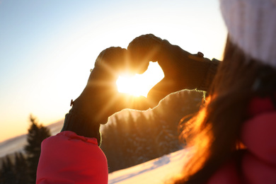 Woman making heart with hands outdoors at sunset, closeup. Winter vacation