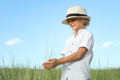 Photo of Cute little boy wearing stylish hat outdoors. Child spending time in nature