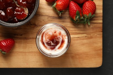 Photo of Tasty yoghurt with jam and strawberries on black table, top view