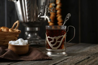 Photo of Glass of tea in vintage holder and samovar on wooden table