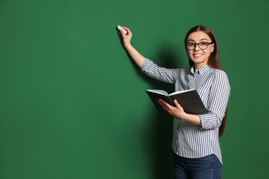 Photo of Portrait of young teacher with book and chalk on green background. Space for text