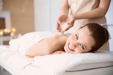 Beautiful young woman having massage with body scrub in spa salon