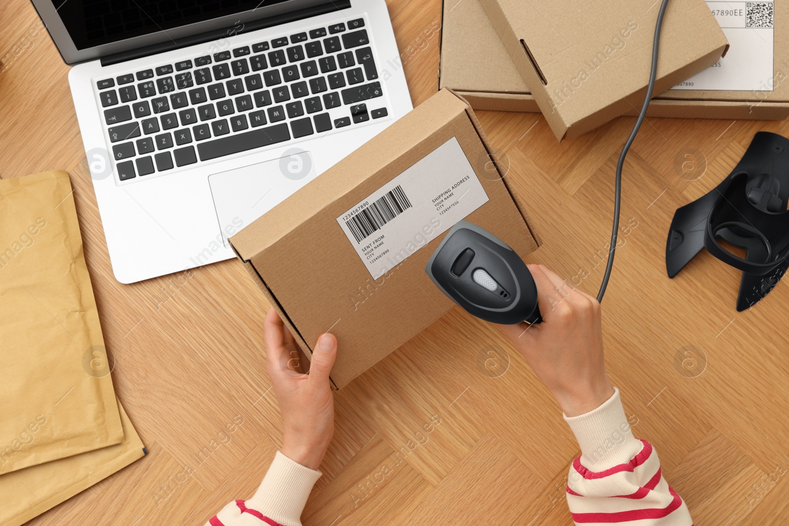 Photo of Woman with scanner reading parcel barcode at wooden table, top view. Online store