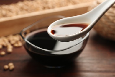 Taking soy sauce with spoon from bowl at wooden table, closeup