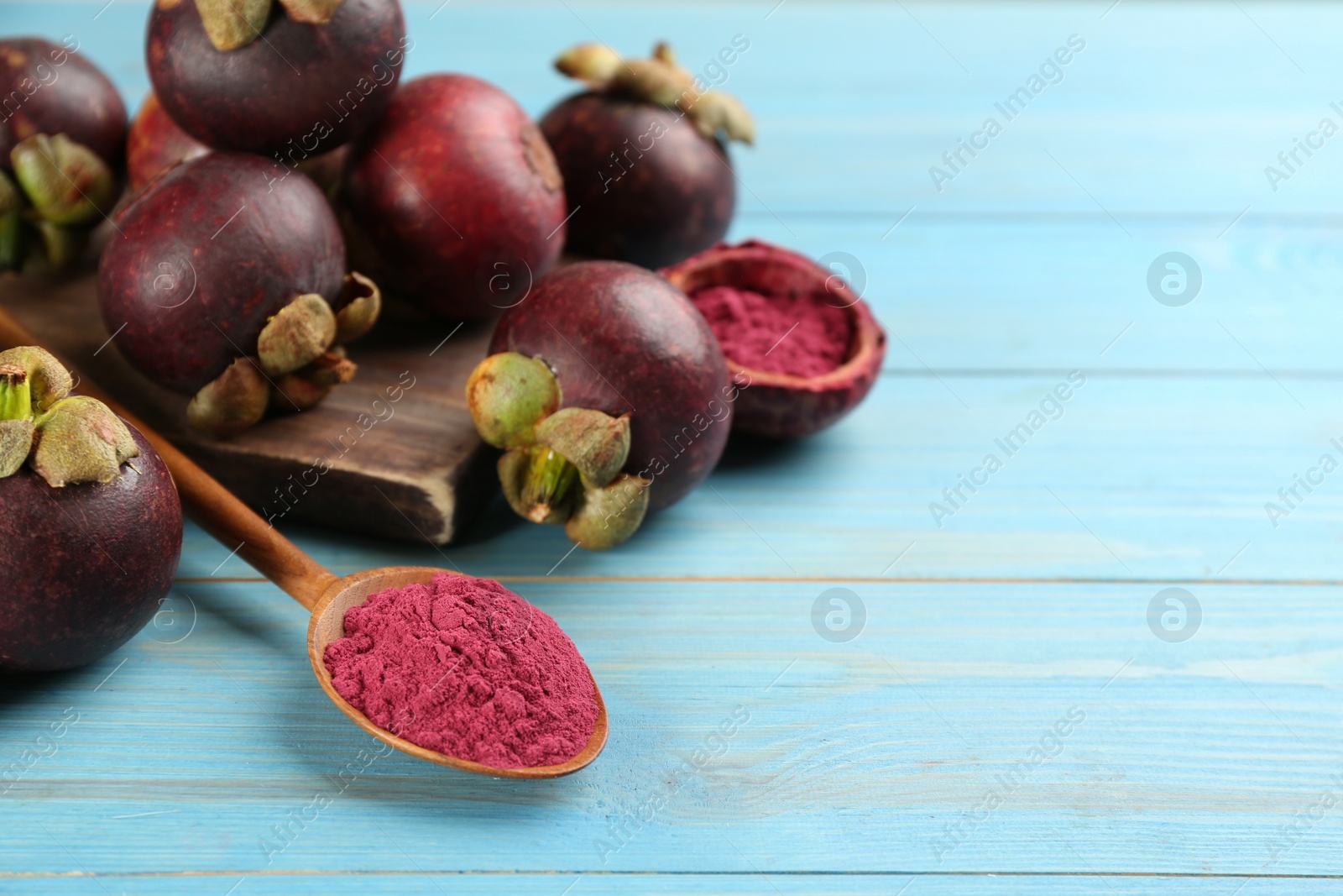 Photo of Purple mangosteen powder and fruits on light blue wooden table. Space for text